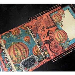 May include: A scrapbook with a steampunk theme featuring hot air balloons, gears, and a raven. The scrapbook has a black background with orange, brown, and blue accents. The text "Scheming Wicked" and "Hunting For" is visible on the scrapbook.