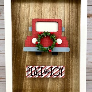 May include: A red toy truck with a green wreath and red berries on the front, and a sign that says "Peace and Joy" in black letters on a red and white striped background.