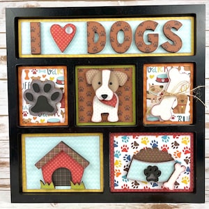 May include: A wooden framed shadow box with the words "I love dogs" in brown letters on a blue background. The box has six smaller squares with various dog-themed images, including a paw print, a dog bone, a dog bowl, and a dog house.