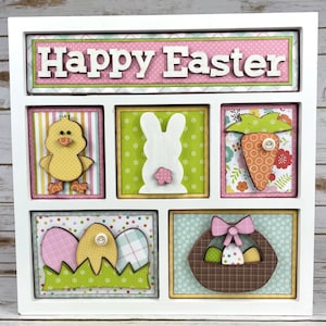 May include: A white wooden box with a pink and green patterned background. The box has six compartments, each with a different Easter-themed image. The top compartment has the text "Happy Easter" in pink letters. The other compartments feature a chick, a bunny, a carrot, a nest with eggs, and a basket of eggs.