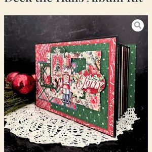 May include: A festive Christmas album kit, labelled "Deck the Halls." The album has a red and green design with a nutcracker and the words "Holly Jolly." It is displayed on a white lace doily. The album is designed for scrapbooking.