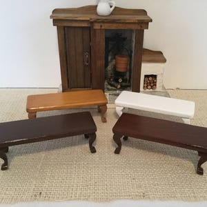 May include: Miniature wooden furniture set featuring four small tables in various colors: dark brown, light brown, and white. The tables have curved legs. A miniature fireplace and a small white pitcher are in the background.