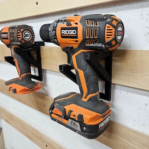 May include: Two orange and black cordless drills with black wall mounts. The drills have the brand name "RIDGID" printed on them. The drill on the right has a battery with the text "2.0Ah High Capacity" printed on it.