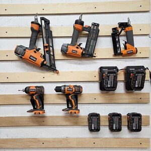 May include: A wall-mounted storage system with various power tools, including a drill, a nail gun, and a saw. The tools are organized on a wooden wall with hooks and shelves. The tools are all black and orange.