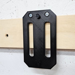 May include: Black plastic wall mount with two slots and three screw holes. The mount is attached to a light wood surface.