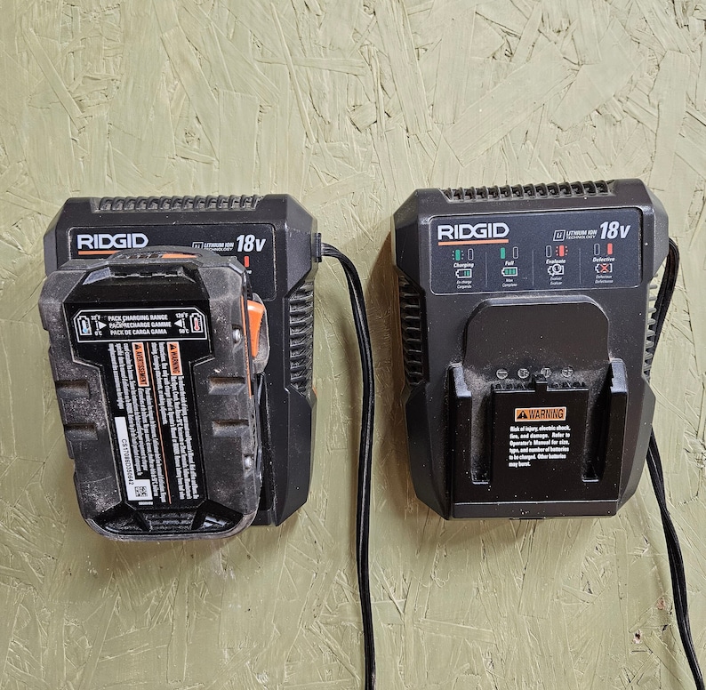 May include: Two black 18V Ridgid battery chargers with a black cord attached to each. The charger on the left has a battery pack attached to it. The charger on the right has a warning label on it.