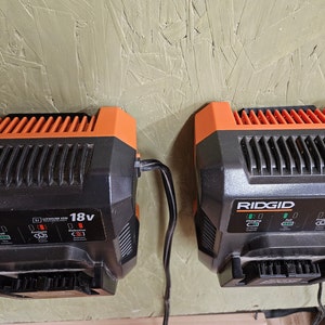 May include: Two black and orange 18V lithium-ion battery chargers with black cords plugged in. The charger on the right has the word "RIDGID" printed on it. The charger on the left has a label that says "LITHIUM ION TECHNOLOGY".