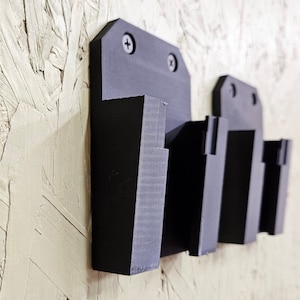 May include: Black wall-mounted organizer with three slots for holding items. The organizer is made of plastic and has a matte finish.