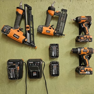 May include: A collection of orange and black power tools, including a nail gun, a drill, and a screwdriver. The tools are all from the brand RIDGID and have different voltage ratings. There are also several batteries for the tools.