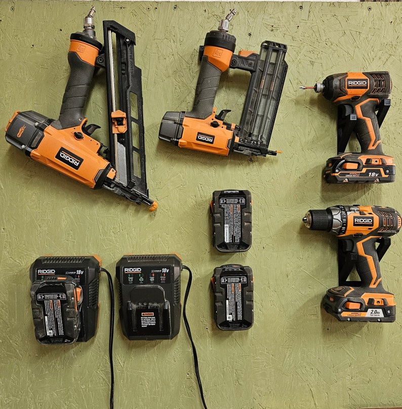 May include: A collection of orange and black power tools, including a nail gun, a drill, and a screwdriver. The tools are all from the brand RIDGID and have different voltage ratings. There are also several batteries for the tools.