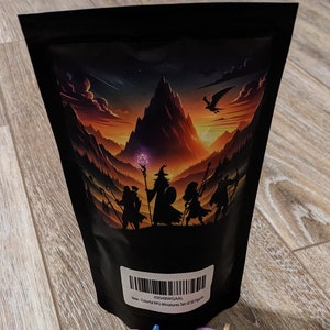 Pode incluir: Um saco de 50 figuras em miniatura de pl&aacute;stico coloridas para jogos de RPG. O saco tem um fundo preto com uma ilustra&ccedil;&atilde;o de fantasia de uma cordilheira e um grupo de aventureiros. O saco est&aacute; etiquetado "Novo - Conjunto de 50 miniaturas RPG coloridas" e tem um c&oacute;digo de barras. As figuras est&atilde;o espalhadas sobre uma superf&iacute;cie de madeira.