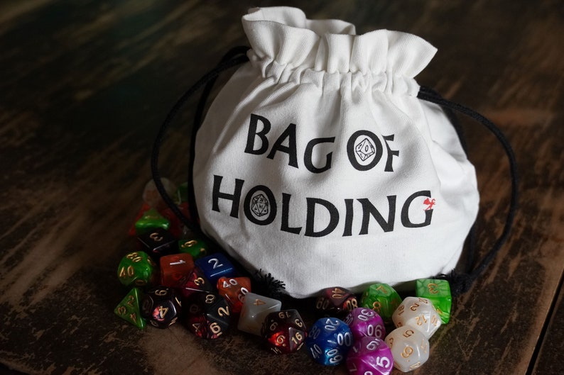 Pode incluir: Uma bolsa de tecido branca com o texto "Bag of Holding" impresso nela. A bolsa est&aacute; cheia de dados coloridos, incluindo vermelho, verde, azul e branco.