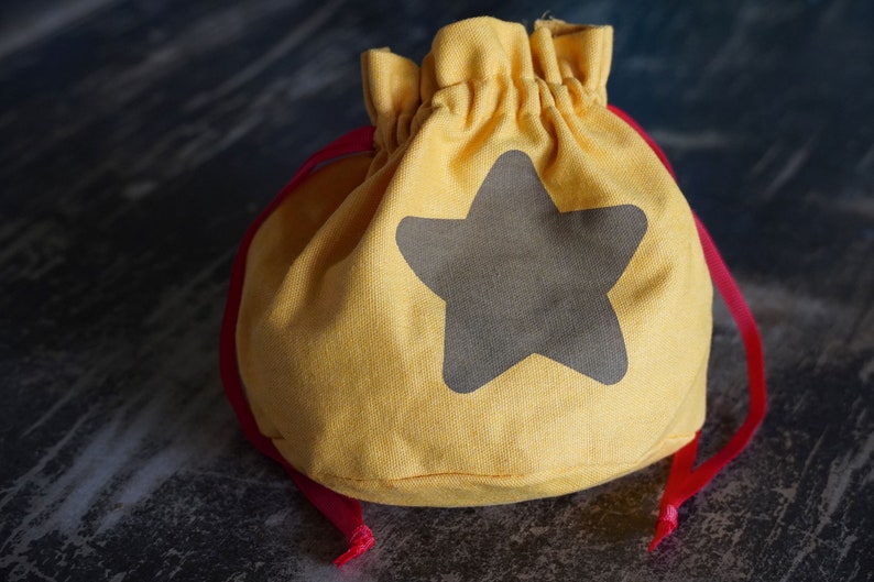 Pode incluir: Uma bolsa de cord&atilde;o amarela com um design de estrela cinza. A bolsa tem um cord&atilde;o vermelho.