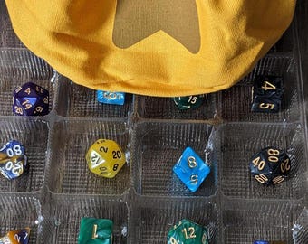 May include: An advent calendar featuring a yellow drawstring bag and an assortment of colourful polyhedral dice. The dice are arranged in a clear plastic tray, with numbers displayed. The calendar displays the numbers 14, 15, and 16.