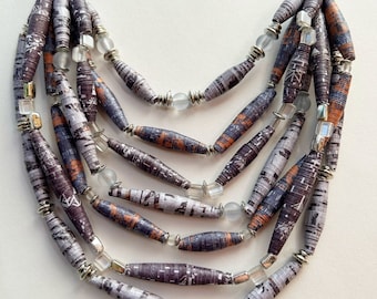 May include: A multi-strand necklace made of rolled paper beads in shades of gray and brown with silver and clear glass accents.
