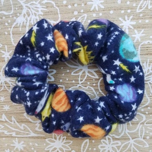 May include: A navy blue scrunchie with a space-themed print featuring planets, stars, and a comet.