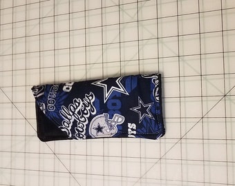 May include: A blue and black fabric phone case with a Dallas Cowboys theme. The case features the team's logo, stars, and the words "Dallas Cowboys".