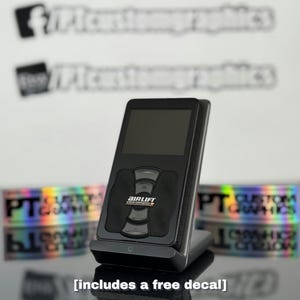 May include: A black Airlift Performance Series air suspension control unit with a digital display and a series of buttons. The unit is on a black stand and includes a free decal.