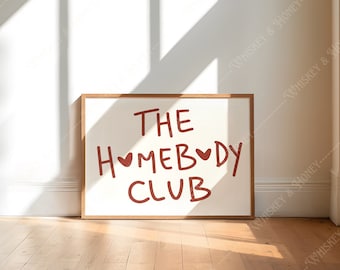 May include: A framed print with a white background and brown frame. The print features the text "THE HOMEBODY CLUB" in red with two small red hearts.