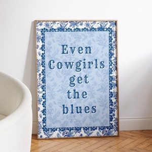 May include: A blue and white framed print with a floral border. The print features the text "Even Cowgirls get the blues" in a blue font.