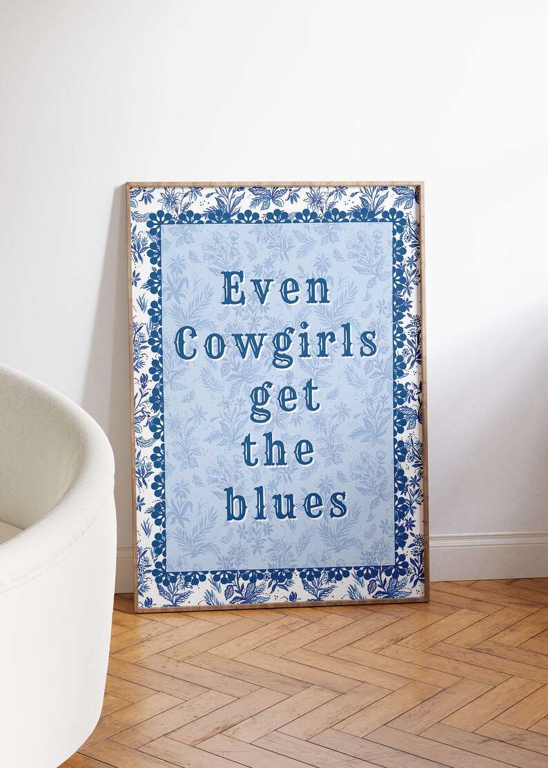 May include: A blue and white framed print with a floral border. The print features the text "Even Cowgirls get the blues" in a blue font.