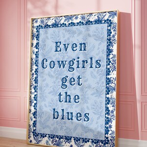 May include: A framed blue and white floral print with the text "Even Cowgirls Get the Blues" in a navy blue font.