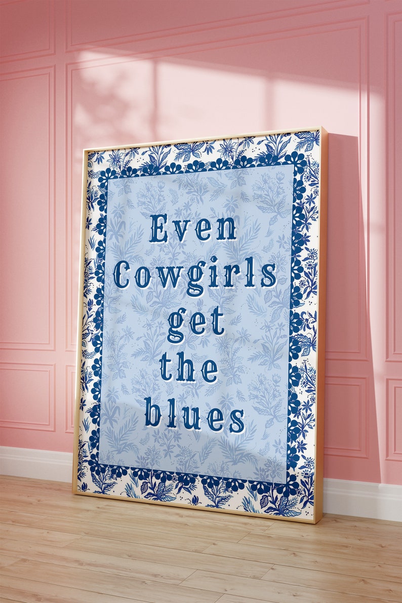 May include: A framed blue and white floral print with the text "Even Cowgirls Get the Blues" in a navy blue font.
