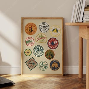 Op de afbeelding: Een ingelijste print met een verzameling vintage kamppeches. De patches zijn cirkelvormig en rechthoekig, met verschillende ontwerpen zoals beren, bomen en tekst als "Camp Wolverine" en "Boy Scouts". Het kleurenpalet omvat rood, groen en blauw.