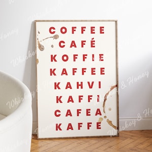 Może przedstawiać: Biały wydruk w ramie z napisem "COFFEE" w czerwonych literach, po którym następują słowa "CAFÉ", "KOFFIE", "KAFFEE", "KAHVI", "KAFFI", "CAFEA" i "KAFEE" w czerwonych literach. Wydruk ma brązowe plamy od kawy.