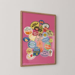 Puede incluir: Una impresi&oacute;n enmarcada que presenta una colecci&oacute;n de pegatinas de frutas vintage sobre un fondo rosa vibrante. Las pegatinas muestran varias frutas como naranjas, pl&aacute;tanos y melocotones, con textos como "Maduro", "Fresco" y "Cuties". El marco es de color madera natural.