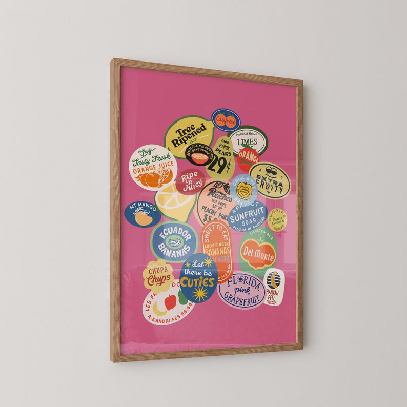 Puede incluir: Una impresi&oacute;n enmarcada que presenta una colecci&oacute;n de pegatinas de frutas vintage sobre un fondo rosa vibrante. Las pegatinas muestran varias frutas como naranjas, pl&aacute;tanos y melocotones, con textos como "Maduro", "Fresco" y "Cuties". El marco es de color madera natural.
