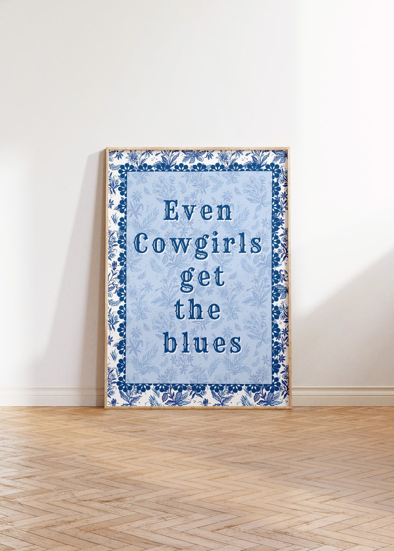 May include: A framed print with a blue and white floral border. The text inside the frame reads "Even Cowgirls get the blues".