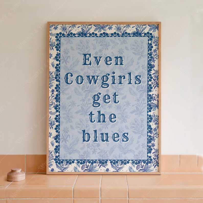 May include: A framed print with a blue floral border and the text "Even Cowgirls get the blues" in blue lettering on a light blue background.