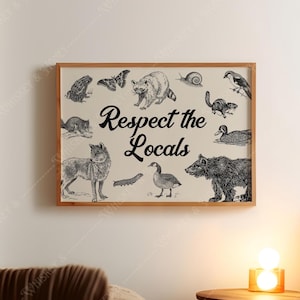 May include: A framed print featuring a collection of detailed black and white illustrations of various animals, including a wolf, bear, and raccoon. The phrase "Respect the Locals" is written in black script across the center of the print.