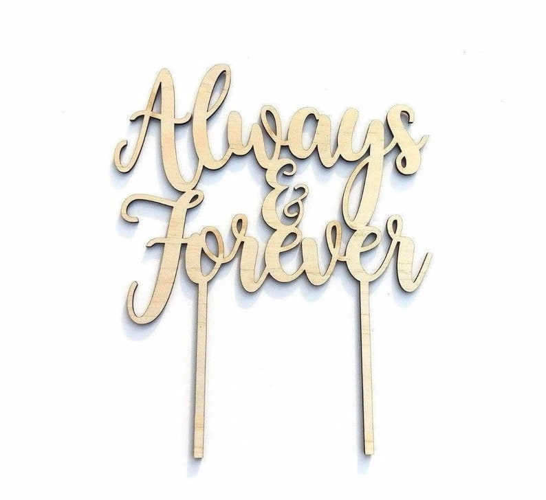 May include: A wooden cake topper with the words "Always & Forever" in a cursive font. The topper has two stakes for insertion into a cake. The wood is a light, natural color.