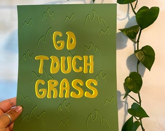 Könnte beinhalten: Ein grüner Druck mit dem Text "GO TOUCH GRASS" in Gelb. Der Druck hat einen grünen Hintergrund mit einem Muster aus grünen Grashalmen.