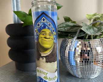 Puede incluir: Una vela azul y blanca con un diseño de vitral que presenta a Shrek, un ogro verde, con el texto "Saint Shrek".