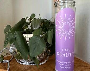 Könnte beinhalten: Eine violette Glaskerze mit einem weißen Sonnenstrahlen-Design und dem Text "I AM BEAUTY encompassing inner self create harmony inspire grace".