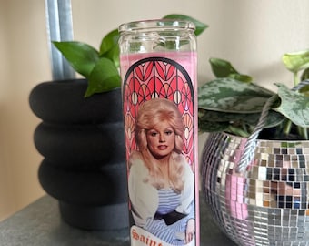 Könnte beinhalten: Rosa farbene Glaskerze mit einem Buntglasdesign, das ein Porträt von Dolly Parton zeigt. Die Kerze trägt den Text "Saint Dolly" auf der Vorderseite.