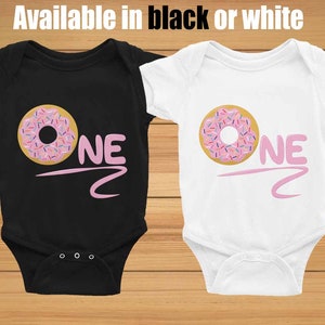 May include: Two baby onesies, one black and one white, with a pink donut and the word "ONE" printed on them.