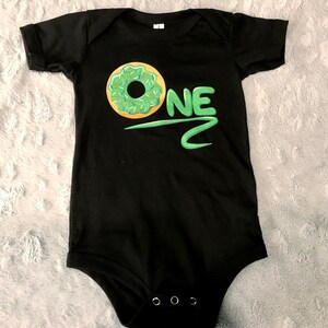 May include: Black baby onesie with a green and yellow donut and the word "ONE" in green.