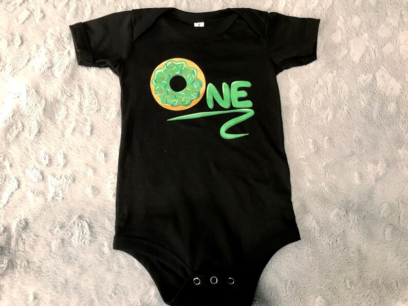 May include: Black baby onesie with a green and yellow donut and the word "ONE" in green.