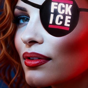 May include: Close-up of a person's face with red hair and bright red lipstick. A black eye patch covers one eye, with the words "FCK ICE" in white letters on a pink background.