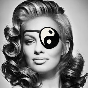 May include: A woman with styled blonde hair is wearing a black eye patch with a white yin yang symbol.