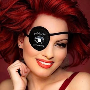 May include: A black circular eye patch featuring a white graphic of an eye and the text I'VE GOT MY EYE ON YOU in white lettering. The patch is secured with a thin black elastic strap that wraps around the head.