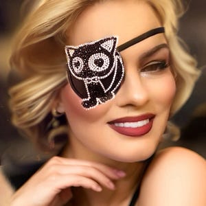 May include: A woman with blonde hair is wearing a black eye patch with a rhinestone cat design. The eye patch is secured with a black strap.