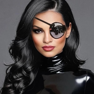 May include: A black eye patch featuring a circular mesh base adorned with dark, shimmering sequins and a small red accent bead. The patch is secured with a thin black elastic strap that wraps around the head, resting over the left eye area.