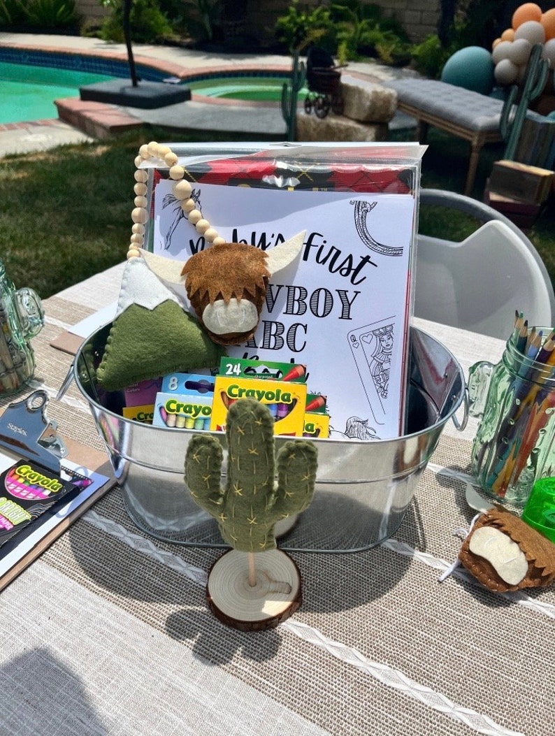 May include: A metal bucket filled with crayons, a felt cactus, a felt highland cow, and a colouring page that says "Baby's First Cowboy ABC".