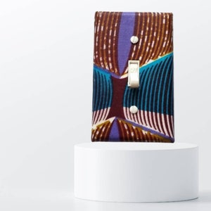 May include: A light switch cover with a colorful geometric pattern in shades of brown, purple, teal, and white. The switch cover is made of fabric and has a silver toggle switch.
