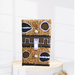 May include: A light switch cover with a brown and black patterned design featuring geometric shapes and a white "OFF" toggle switch.